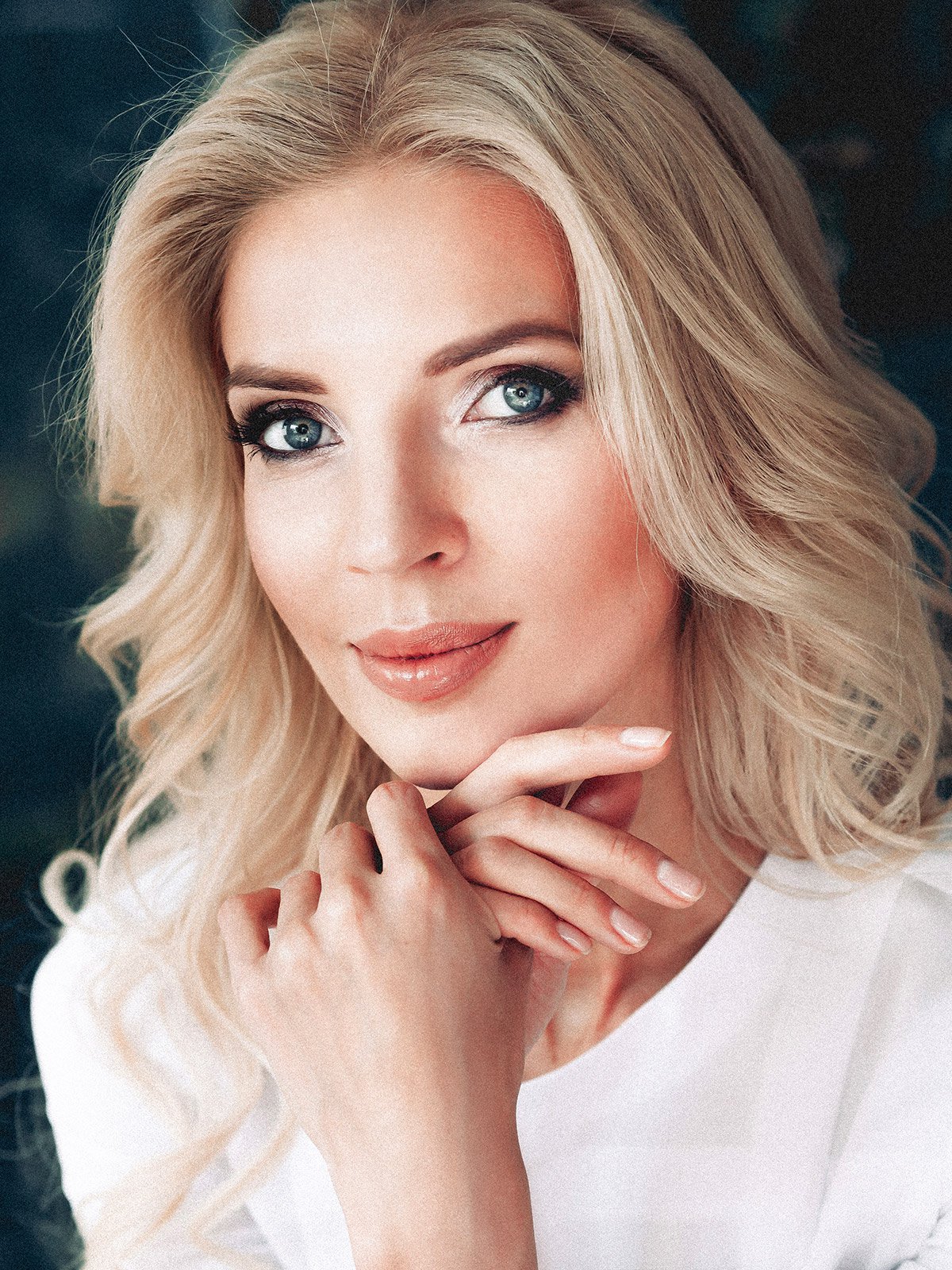 blonde lower blepharoplasty patient model in a white top resting her chin on her hands